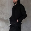 Brutal handsome young hipster man with a beard in a black stylish sweatshirt with a hood in black trendy jeans posing Royalty Free Stock Photo