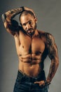 A brutal Latin American or Cuban with tattoos on his body poses on a gray background. Studio portrait