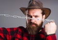Brutal man in cowboy hat with chain. Serious bearded male in plaid shirt trying to break metal chains.