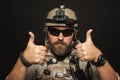 Brutal man in military desert uniform and body armor shows two fingers up on black background in Studio. The bearded player in the