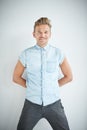 Brutal man with a small beard is leaning on the wall , wearing a blue short-sleeved shirt and gray pants , hands are Royalty Free Stock Photo