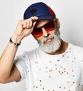 Brutal senior rich man in designer t-shirt holds the visor of his blue and red baseball cap stylish fashionable men