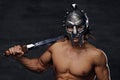 A man in a silver gladiator helmet holds an iron sword.