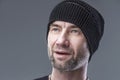 Brutal unshaven man in a black knitted hat. Grey background. Close-up