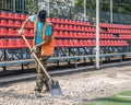 A brutal unshaven worker in overalls smooths gravel for asphalt in a treadmill stadium. Hard work with a shovel in hot weather