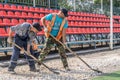 A brutal unshaven worker in overalls smooths gravel for asphalt in a treadmill stadium. Hard work with a shovel in hot weather