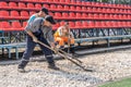 A brutal unshaven worker in overalls smooths gravel for asphalt in a treadmill stadium