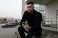 brutal young man in a black coat with a mobile phone on the background of the office center Royalty Free Stock Photo