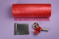 Bubble wrap roll, padded envelope and tape dispenser on lilac background, flat lay