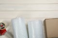 Bubble wrap rolls, cardboard box and tape dispenser on white wooden background, flat lay. Space for text Royalty Free Stock Photo