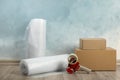 Bubble wrap rolls, tape dispenser and boxes on floor near light blue wall Royalty Free Stock Photo