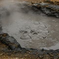 Bubbling mud pool with a dark, viscous surface, releasing steam. The surrounding Royalty Free Stock Photo