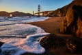 Bubbling seafoam on shore with sunset striking Golden Gate Bridge from sandy beach