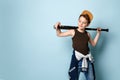 Teenage boy in cap, undershirt, jeans and hoodie tied around his waist. Holding black baseball bat, posing on blue background Royalty Free Stock Photo