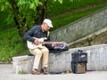 Senior street artist musician sitting on a bench in the park and playing at an electric guitar Royalty Free Stock Photo