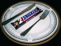 Snickers chocolate bar on a plate next to a fork and a knive