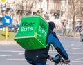 Uber eats courier on a bicycle carrying the green delivery bag. Young adult delivering the order