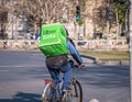 Uber eats courier on a bicycle carrying the green delivery bag. Young adult delivering the order