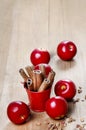 Bucket of cinnamon sticks on wooden table. Red apples around