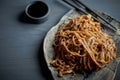 Buckwheat noodle with teriaki sauce.Asian dish. With wooden sticks. On a clay plate and a gray background. Royalty Free Stock Photo