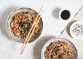 Buckwheat noodles with vegetables and meat decorated with sesame and seaweeds in bowls on grey background. Top view Royalty Free Stock Photo