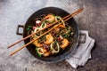 Buckwheat stir-fry noodles with seafood - shrimps, octopus, squid in cast iron asian wok with cooking chopstick. Top