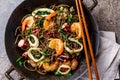 Buckwheat stir-fry noodles with seafood - shrimps, octopus, squid in cast iron asian wok with cooking chopstick. Top
