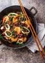 Buckwheat stir-fry noodles with seafood - shrimps, octopus, squid in cast iron asian wok with cooking chopstick. Top