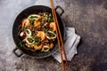 Buckwheat stir-fry noodles with seafood - shrimps, octopus, squid in cast iron asian wok with cooking chopstick. Top