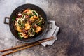 Buckwheat stir-fry noodles with seafood - shrimps, octopus, squid in cast iron asian wok with cooking chopstick. Top