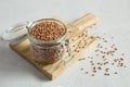 Buckwheat uncooked grains in glass jar on the wooden cutting board close up on the gray background. Healthy, dietary food. Royalty Free Stock Photo