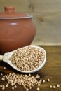 Buckwheat in a wooden spoon, next to a clay pot on a brown wooden background. Royalty Free Stock Photo