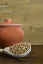 Buckwheat in a wooden spoon, next to a clay pot on a brown wooden background. Royalty Free Stock Photo