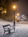 Budapest, Hungary - Bench And Lamp Post In A Snowy Park At Buda District With Szechenyi Chain Bridge At Background During Snowing