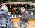Senior man uses mobile phone sitting at table in street cafe with cup of mulled wine. Annual Christmas fair in Budapest