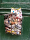 Homemade metal basket with fresh newspapers and magazines on an old front door painted in green