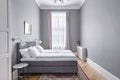 Budapest, Hungary - May 30, 2019: Modern minimal grey bedroom with pastel lilac curtains and red persian rug from side view