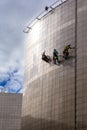 Rope access technicians hanging on the side of a metal high-rise building and cleaning the facade