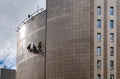 Rope access technicians hanging on the side of a metal high-rise building and cleaning the facade