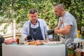 Two caucasian male shefs in Budapest Hungary who prepares a meat dish, Outdoor cooking.