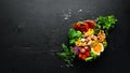 Buddha Bowl: Chicken, chickpeas, broccoli, tomatoes, egg, paprika, onion in a black plate on a black background.