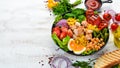 Buddha bowl: Chicken, chickpeas, chickpeas, broccoli, tomatoes, egg, paprika, onion in a black plate on a white wooden background Royalty Free Stock Photo