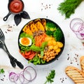 Buddha bowl: pumpkin, broccoli, egg, tomatoes, carrots, paprika in a black plate on a white wooden background. Royalty Free Stock Photo