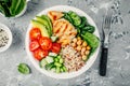 Buddha bowl with spinach salad, quinoa, roasted chickpeas, grilled chicken, avocado, tomatoes, cucumbers, sesame seeds.