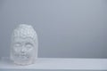 Buddha head statuette on a white table against gray concrete wall copy space Royalty Free Stock Photo
