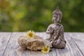 A Buddha statuette and yellow daisy flowers on a aged wooden board