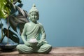 Buddhism religion. Decorative Buddha statue with burning candle, incense stick on wooden table and monstera against light blue Royalty Free Stock Photo