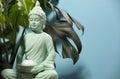 Buddhism religion. Decorative Buddha statue with burning candle and monstera against light blue wall, space for text Royalty Free Stock Photo