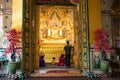 Buddhist family praying in front of the golden Buddha U Kanti. Big golden image of the sitting Buddha. Beautiful wooden door in