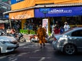 A Buddhist monk dressend in the classical orange saffron robe and a face mask is crossing a street in Bangkok, Thailand